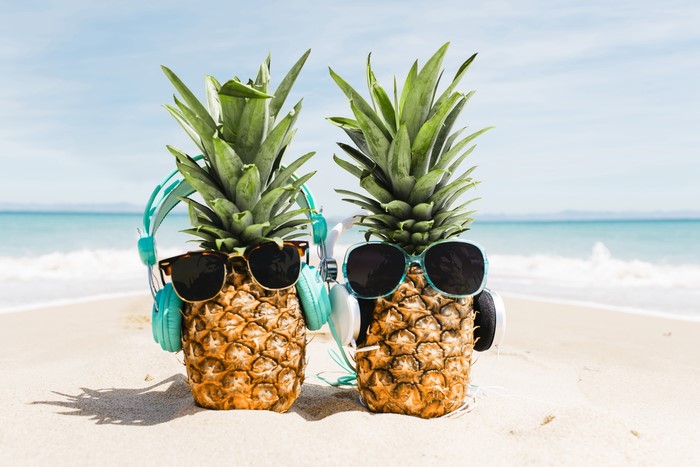 Two pineapples with sunglasses and headphones on a beach