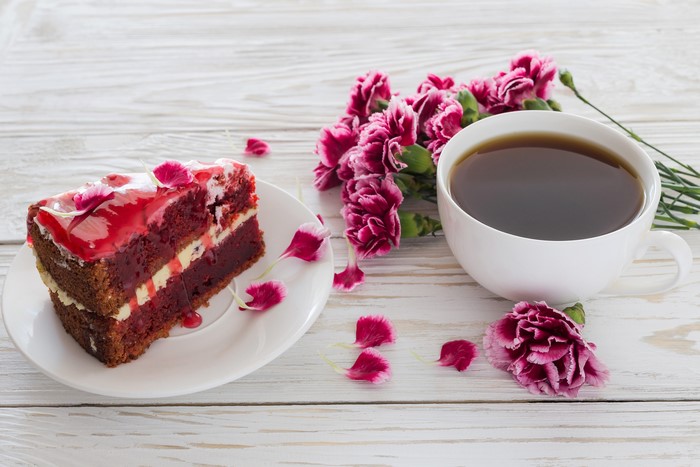 Red velvet cake slice with coffee and carnations