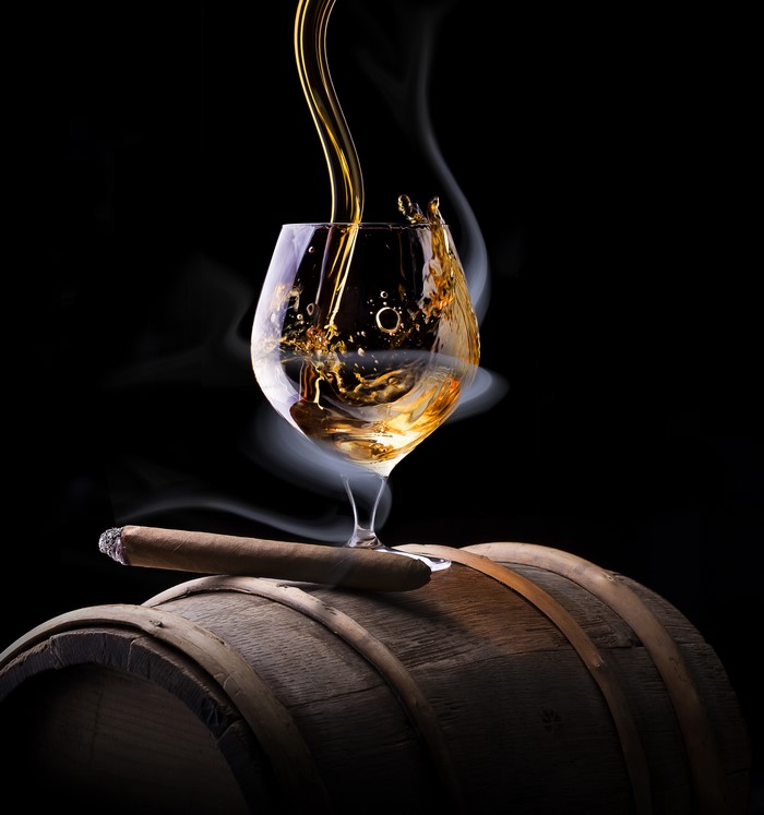 Whisky pouring into a glass with a cigar on a barrel