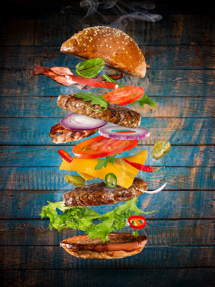 Deconstructed hamburger with flying ingredients on a wooden background