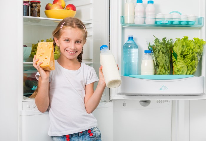 Girl Holding Cheese and Milk in Refrigerator