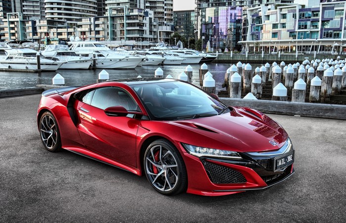 Red Honda NSX parked by a marina with yachts and buildings