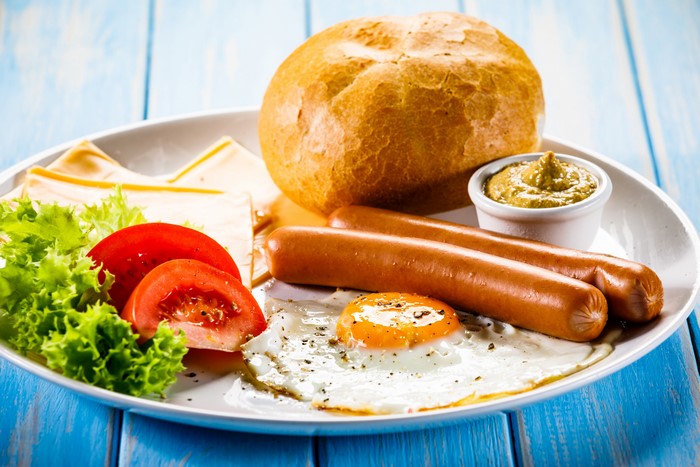 Breakfast plate with sausages, fried egg, bread, tomatoes, and lettuce