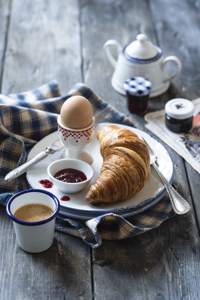 Breakfast with croissant, boiled egg, jam, and coffee