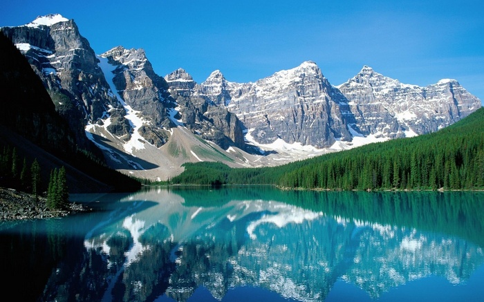 Snow-capped mountains reflected in a turquoise lake with pine trees