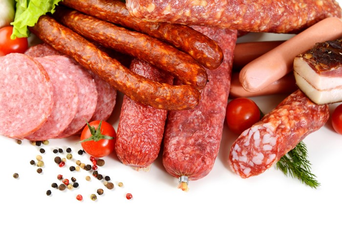 Assortment of sausages, tomatoes, and spices on white background