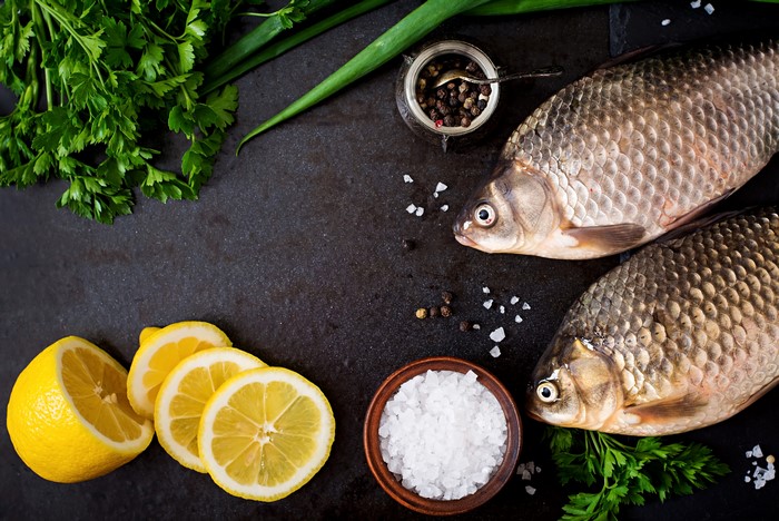 Two raw fish with lemons, parsley, salt, and pepper