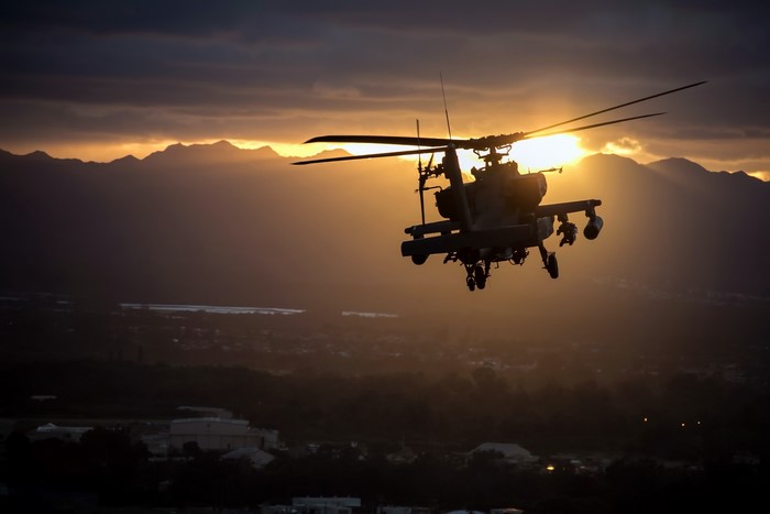 AH-64 Apache helicopter flying at sunset