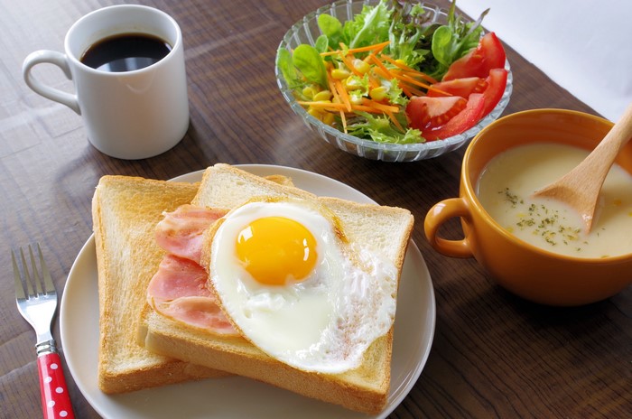 Breakfast with toast, fried egg, bacon, salad, soup, and coffee