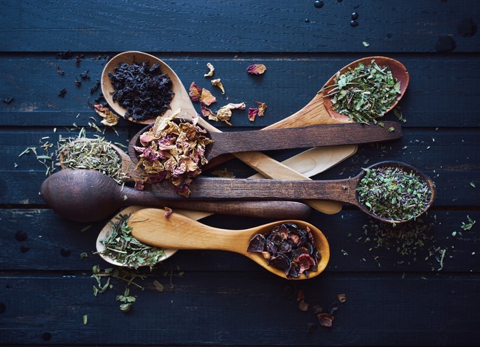 Wooden spoons filled with dried herbs and flowers on dark wood planks
