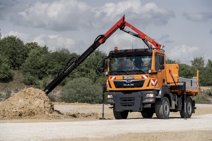 Orange MAN truck with a crane loading dirt