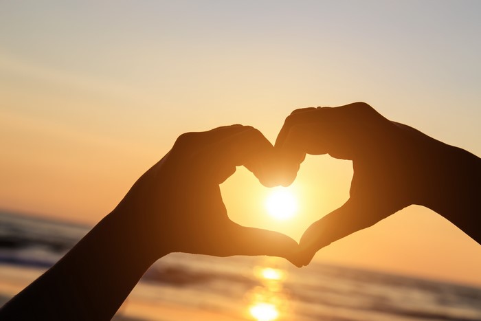 Hands forming a heart shape at sunset
