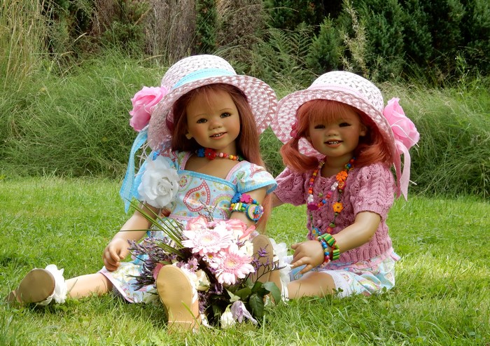 Two dolls in hats with bouquets in a park
