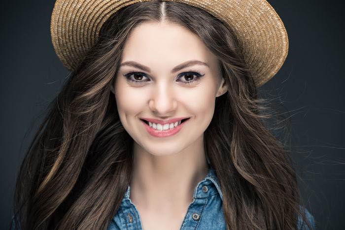 Woman with brown hair wearing a straw hat and denim shirt