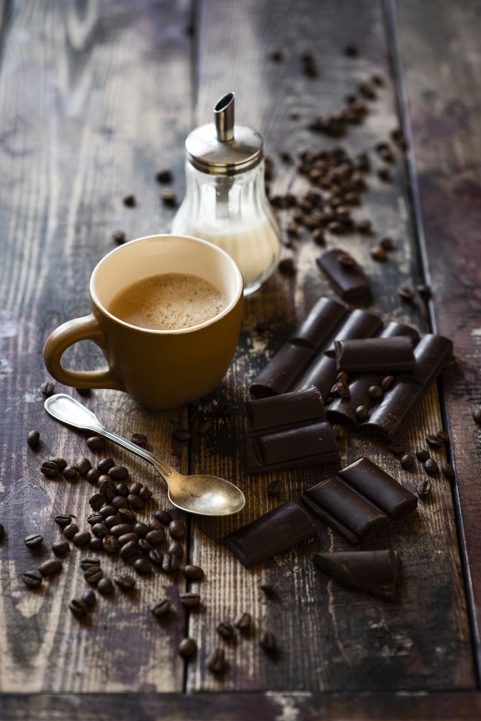 Coffee cup with chocolate and sugar dispenser on wood