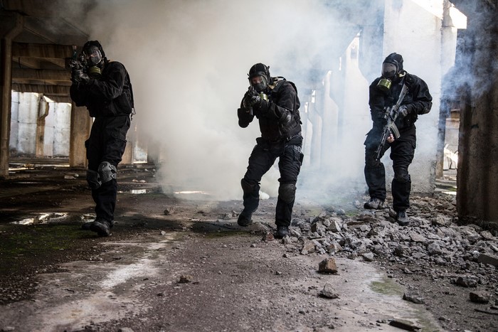 Three soldiers in gas masks with assault rifles in a ruined building