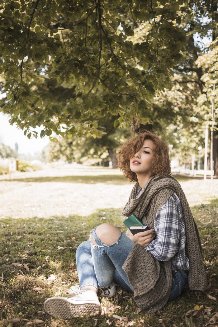 Woman with curly hair sitting in a park with books