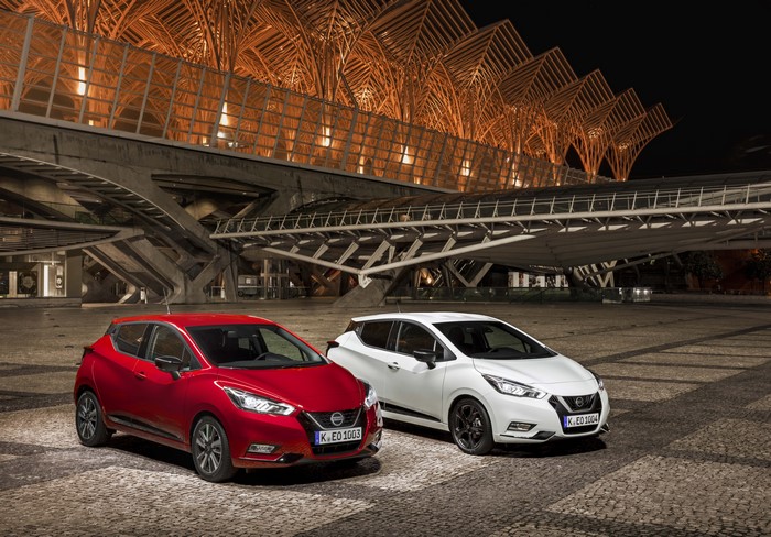 Two Nissan Micra cars in front of a modern building