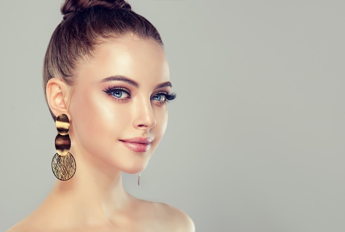 Brunette girl with earrings on gray background