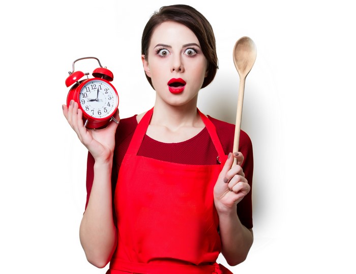 Woman in red apron holding alarm clock and spoon