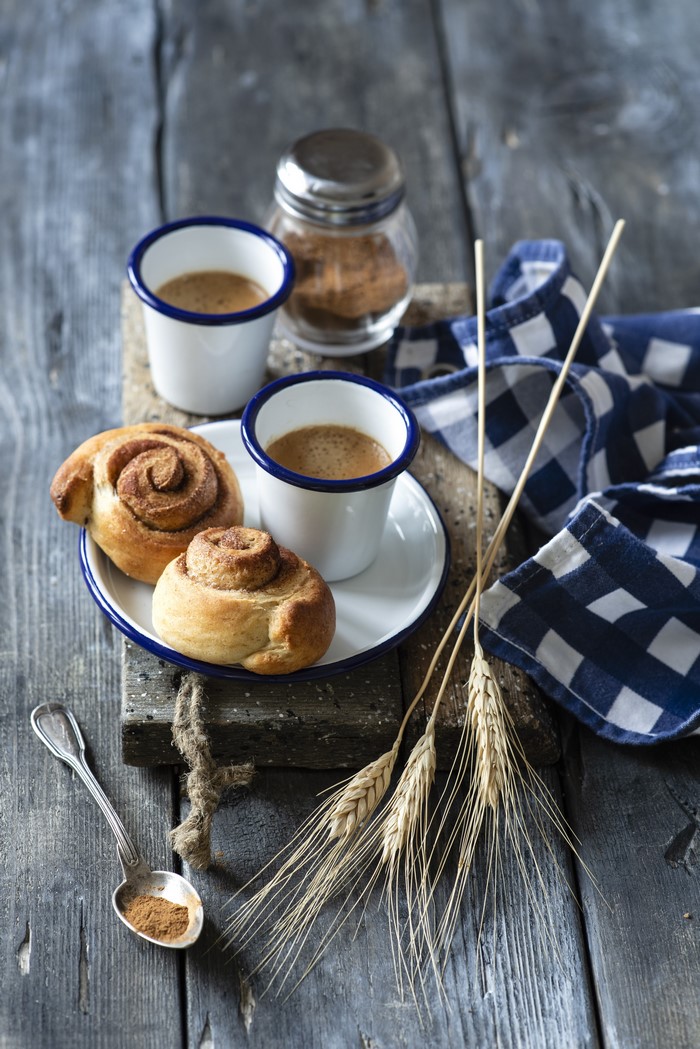 Two cinnamon rolls with coffee and wheat stalks