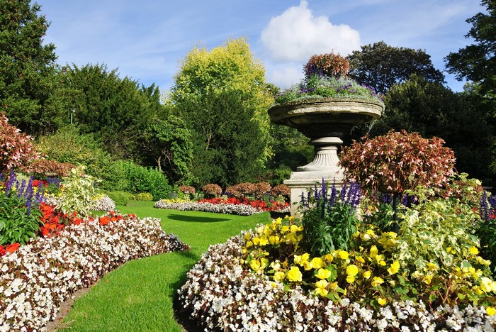 Beautifully manicured park garden with colorful flower beds and a stone urn