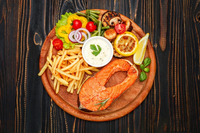 Salmon steak with french fries and vegetables on a cutting board