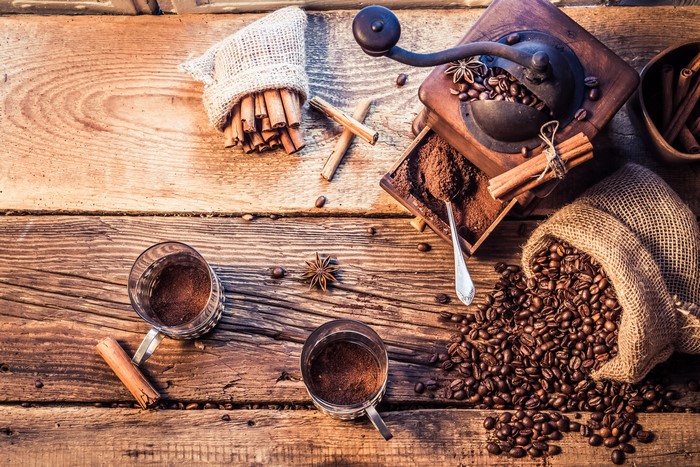 Coffee beans, cinnamon sticks, and coffee mill on wood