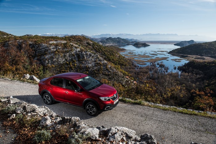 Red Renault Logan Stepway on a mountain road overlooking a lake