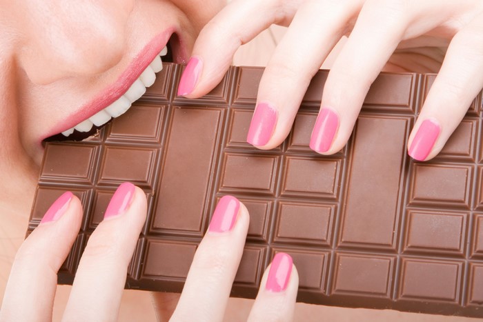 Woman biting chocolate bar with pink nails
