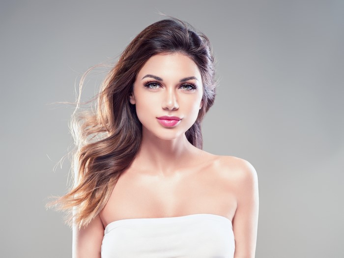 Brown haired woman with wavy hair on gray background