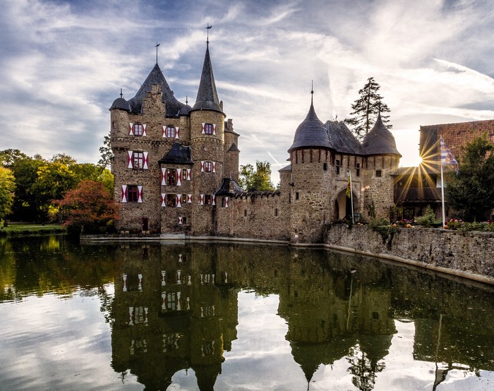 Satzvey Castle reflected in a pond with sun rays