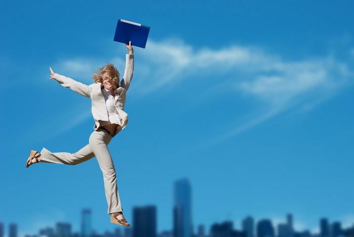 Blonde woman in business attire jumping with a blue folder