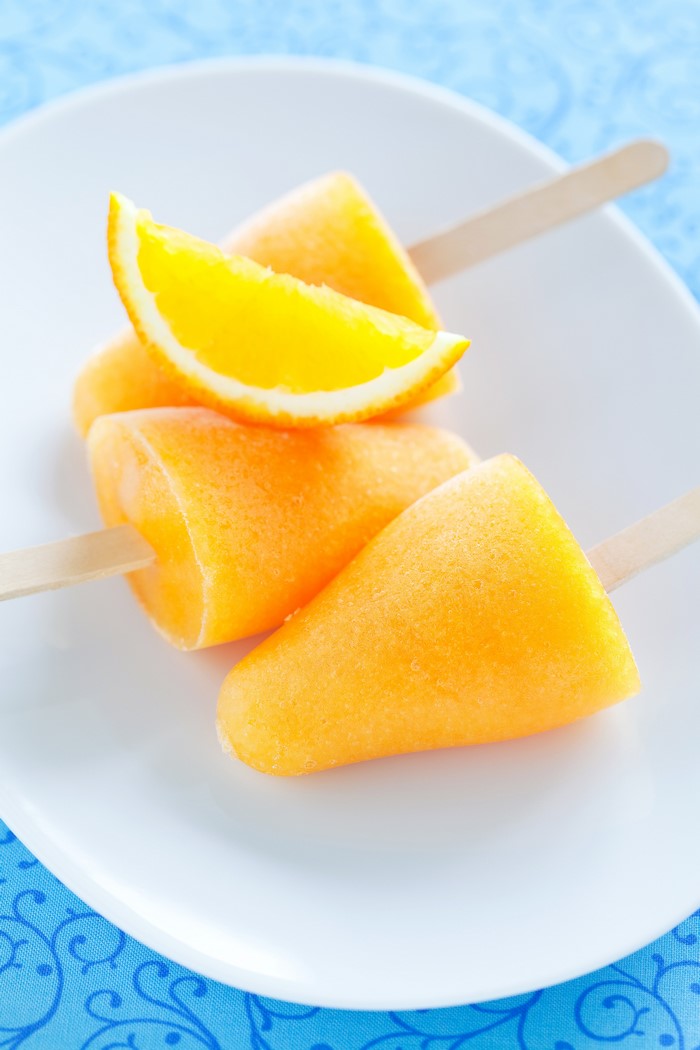 Orange popsicles on a white plate with orange slice