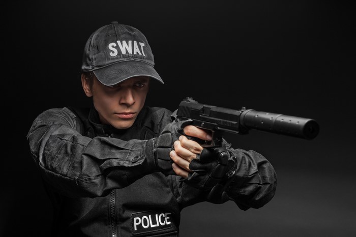 Man in SWAT uniform holding a pistol with suppressor