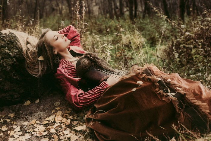 Woman in corset and dress lying on log in forest