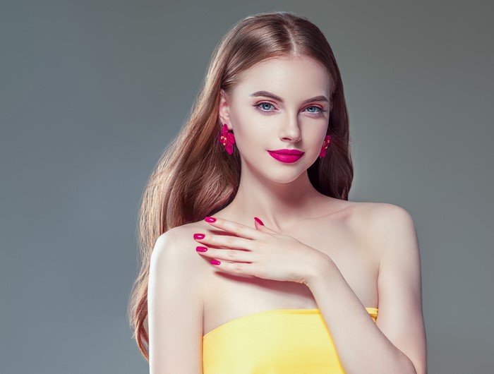 Woman with brown hair, red lips, and pink earrings