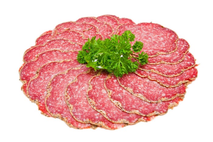 Sliced salami with parsley garnish on white background