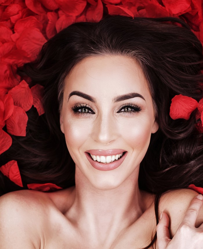 Woman with dark hair lying on red rose petals