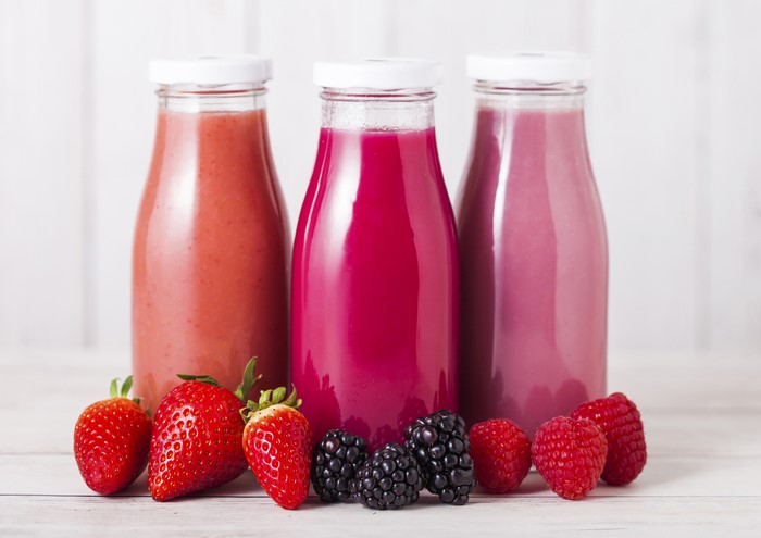 Three bottles of berry juice with strawberries, raspberries, and blackberries
