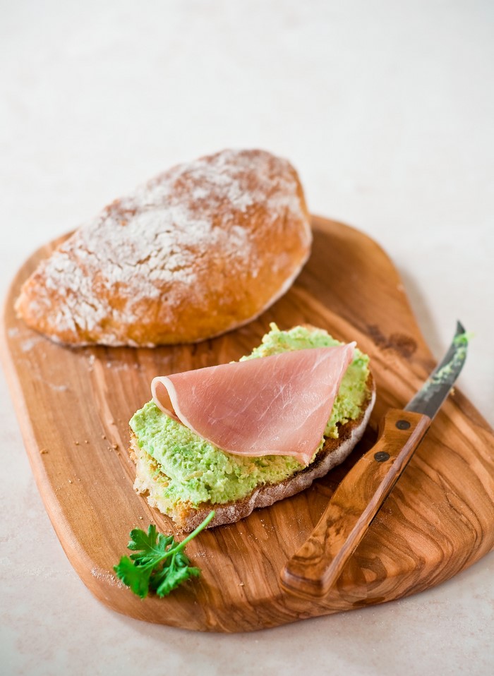 Open-faced sandwich with ham and avocado spread on a wooden board