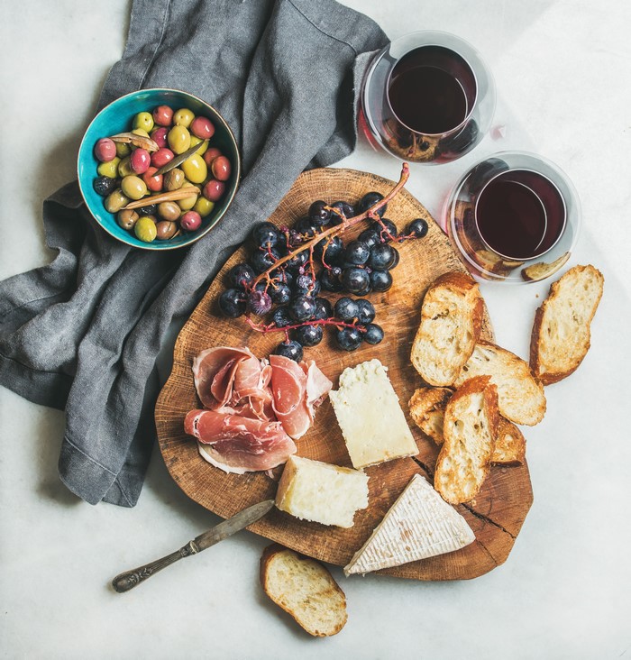 Charcuterie board with cheese, ham, olives, grapes, and bread with wine
