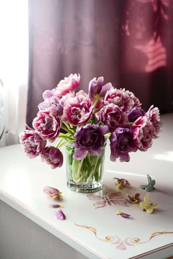 Bouquet of pink and purple tulips in a glass vase with decorative butterflies