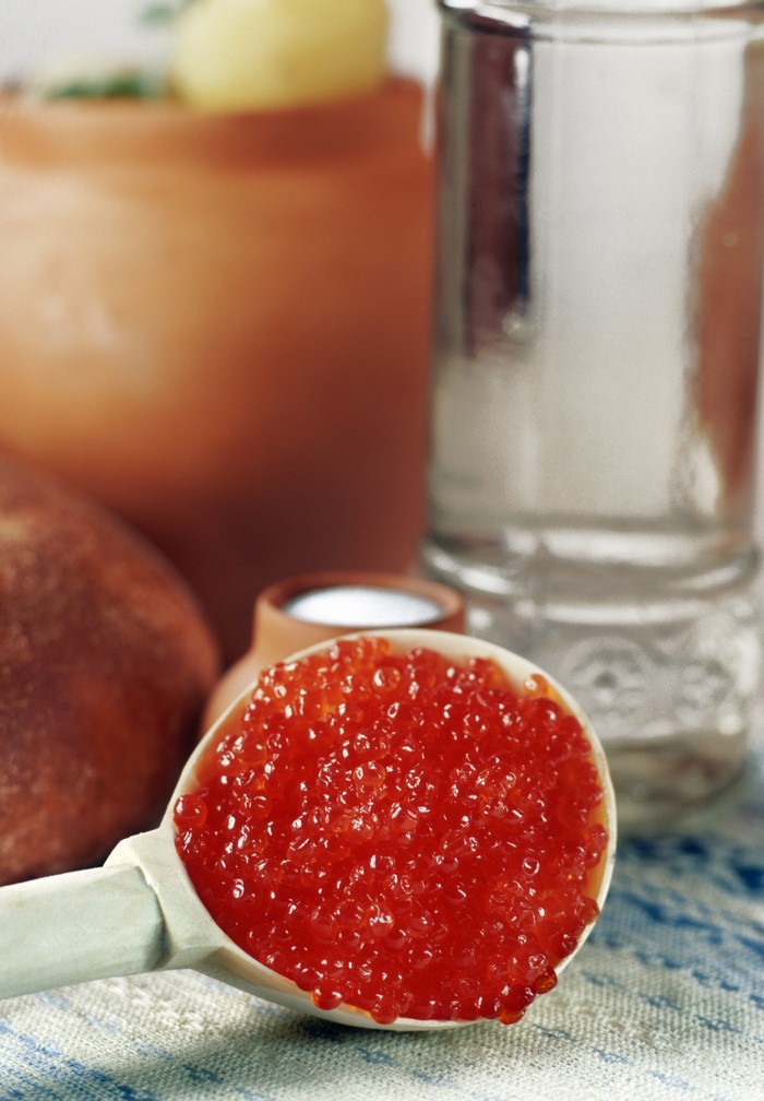 Spoonful of red caviar with clay pot and glass