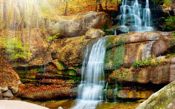 Waterfall cascading over mossy rocks in autumn forest