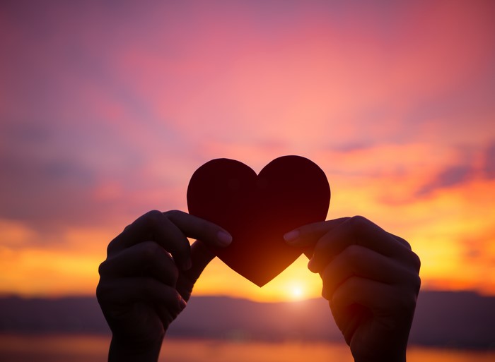 Hands holding a heart silhouette at sunset