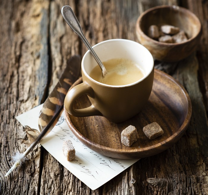Coffee cup with sugar cubes and feather on wood