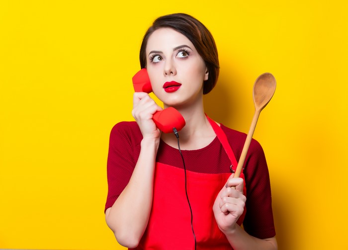 Woman with telephone and spoon on yellow background