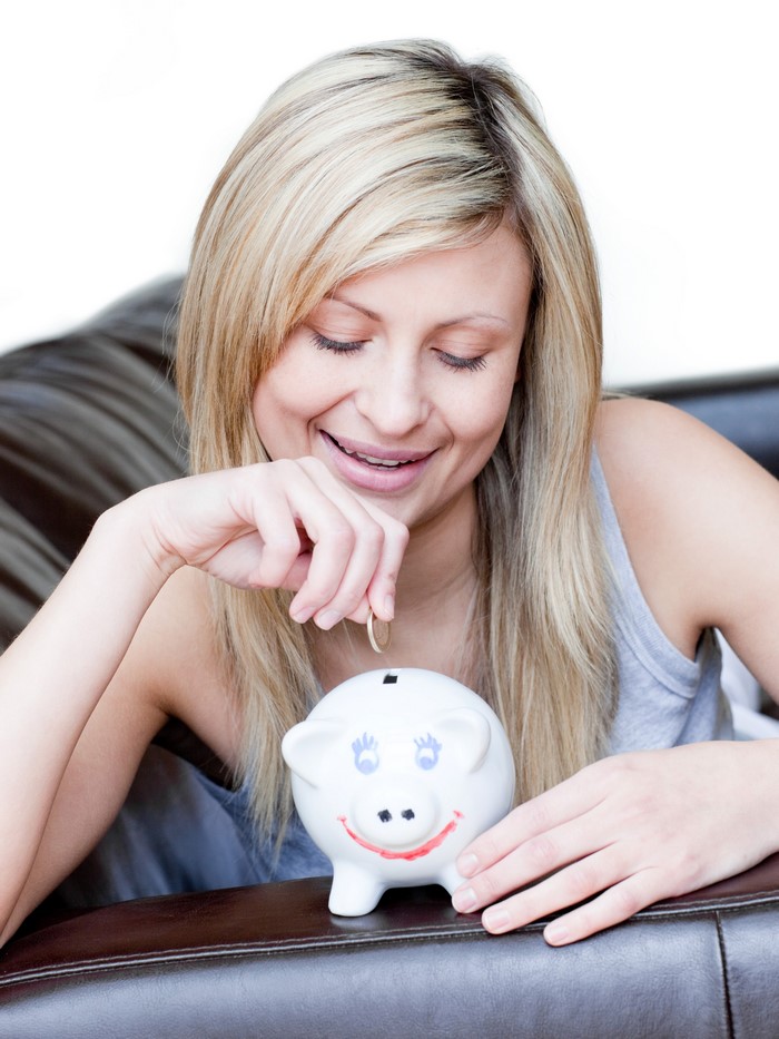 Blonde girl putting coin in piggy bank