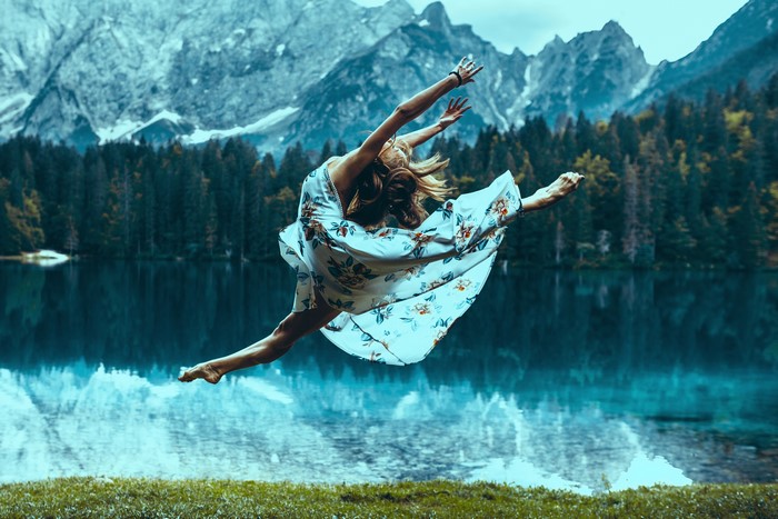 Woman in dress jumping by a lake with mountains